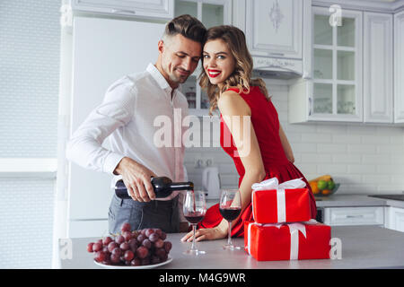 Femme heureuse de faire up smiling to camera pendant que son bel homme de verser le vin dans des verres à la maison sur la célébration Banque D'Images