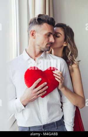 Les jeunes magnifique jeune femme en robe rouge baiser la confiance bel homme et tenant à coeur peluche accueil Banque D'Images