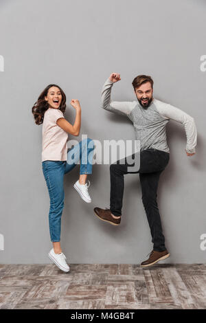 Portrait d'un jeune couple sympathique de célébrer et danser sur fond gris Banque D'Images