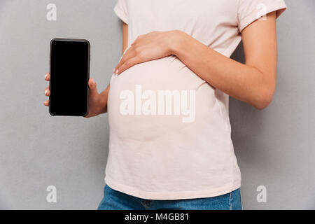 Close up of a pregnant woman's belly avec part montrant écran blanc téléphone sur fond gris Banque D'Images