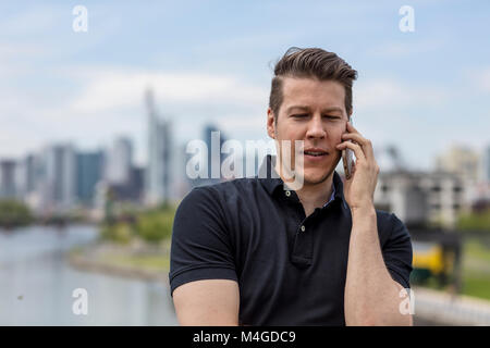 Un homme parlant sur un téléphone mobile et une ville avec des gratte-ciel et immeubles de grande hauteur à l'arrière-plan. Close up shot. Banque D'Images