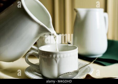 Servir le lait dans une tasse en céramique blanche à partir d'un pot en céramique blanche sur un tableau statistique Banque D'Images
