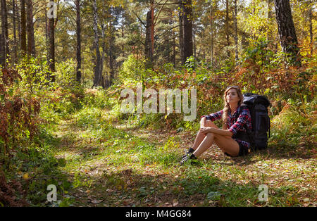 Blonde jeune fille de tourisme avec un sac à dos assis en marge de la sentier de forêt. La Russie, la Sibérie, Salair Banque D'Images