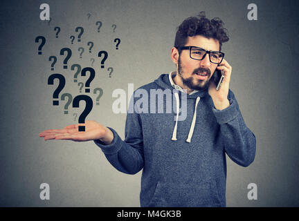 L'incompréhension et l'appel lointain. Les jeunes en colère man talking on mobile phone a beaucoup de questions isolé sur fond gris. Banque D'Images