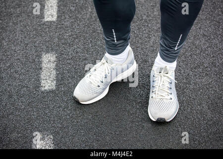 Dans les jambes de couleur gris chaussures de course comité permanent sur l'asphalte. Banque D'Images