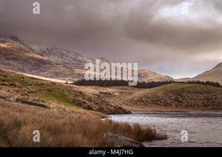 Vue sur le lac à la Snowdon Horseshoe à Llyn Y Dywarchen, comme le soleil illumine le côté montagne dans le parc national de Snowdonia, le Pays de Galles. Banque D'Images