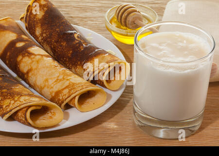 Fédération des crêpes au miel sur une assiette et un verre de lait frais sur une table en bois de chêne Banque D'Images