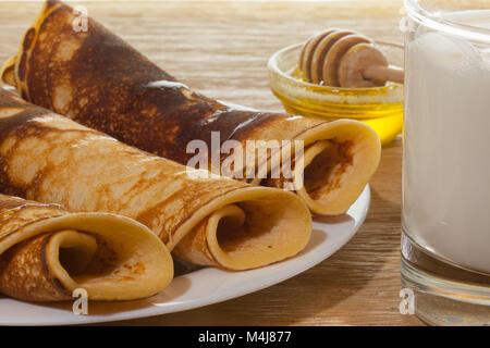 Fédération des crêpes au miel sur une assiette et un verre de lait frais sur une table en bois de chêne Banque D'Images