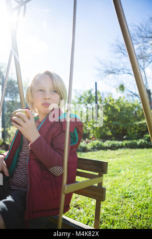 Boy relaxing in swing sur une journée ensoleillée Banque D'Images