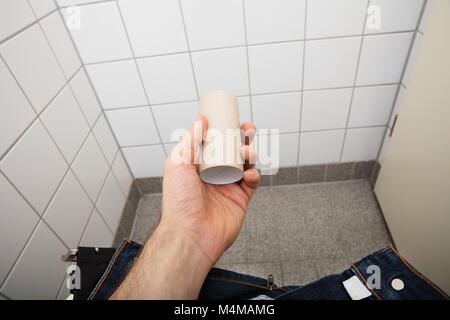 Close-up of a Man's Hand Holding Rouleau de papier toilettes vides dans la salle de bains Banque D'Images