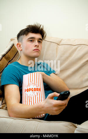 Teenage boy sur un sofa eating popcorn Banque D'Images