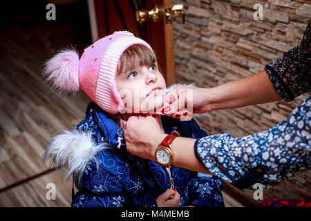 Mère d'habiller ma petite fille et lier son chapeau. Banque D'Images