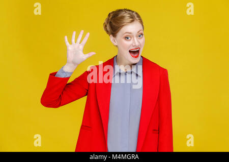 Bonjour ! Ginger red head business woman in red suit montrant hi signe. Studio shot, isolé sur fond jaune Banque D'Images