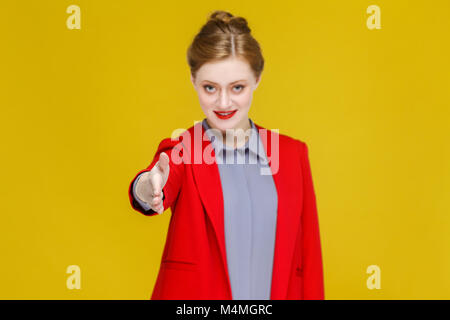 Poignée de mains ! Ginger red head business woman in costume rouge montrant une liaison signe. Studio shot, isolé sur fond jaune Banque D'Images