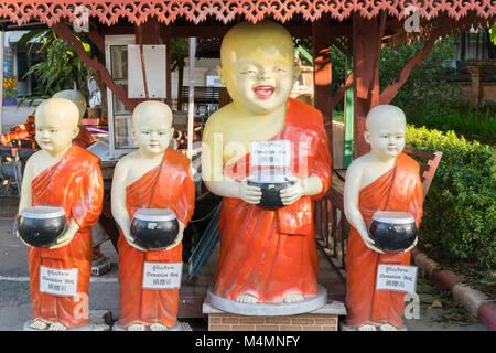 Thaïlande - CHIANG MAI Le 29 janvier 2018 ; quatre statues de moines novices bouddhistes smiling holding alms conteneurs avec enseignes de don Banque D'Images