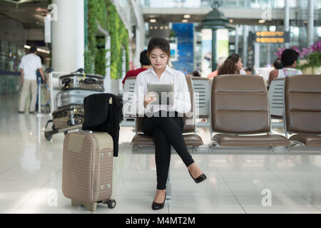 Jeune femme asiatique passager à l'aéroport, en utilisant son ordinateur tablette en attendant son vol dans le terminal à l'aéroport. Banque D'Images