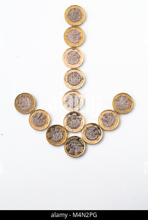 Un nouveau British pound coins disposés pour former la forme d'une flèche orientée vers le bas, indiquant une faible performance par la monnaie sur les marchés des changes Banque D'Images