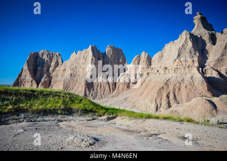 Vue horizontale de Painted Desert dans Badlands National Park montre des couches de ciel ensoleillé bleu vif, rouge et blanc à rayures hills, Green grass, et de graves Banque D'Images