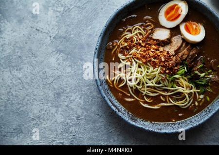 Ramen japonais avec les poitrines de porc, champignons et œufs marinés servis en bleu Bol en céramique fait main garni de ciboulette Banque D'Images
