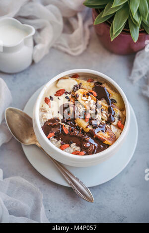 Bol de porridge surmonté de bananes caramélisées, chocolat fondu, le cacao nibs, les baies de goji et de tournesol Banque D'Images