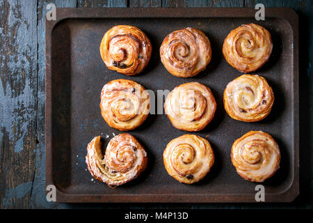 Des vitrages feuilletés à la cannelle avec de la crème anglaise et les raisins secs sur un plat à four plus vieux bleu foncé fond de bois. Vue d'en haut. Style rustique Banque D'Images