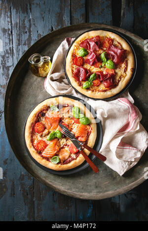 Deux pizza traditionnelle avec bresaola, saumon fumé, fromage, tomates et basilic servi sur grand plateau vintage avec de l'huile d'olive et la cuisine serviette sur the w Banque D'Images