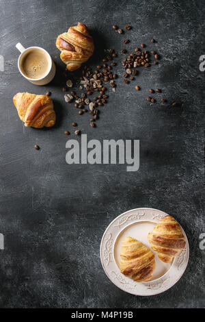 Les frais croissants sur la plaque vintage blanc et tasse de café expresso, café en grains, le sucre sur noir texture background. Vue de dessus, la CDP Banque D'Images