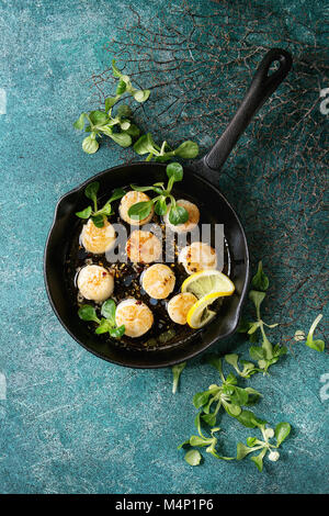 Pétoncles poêlés au beurre citron sauce épicée en fonte pan servie avec une salade verte sur fond texture turquoise. Vue de dessus, copy space Banque D'Images