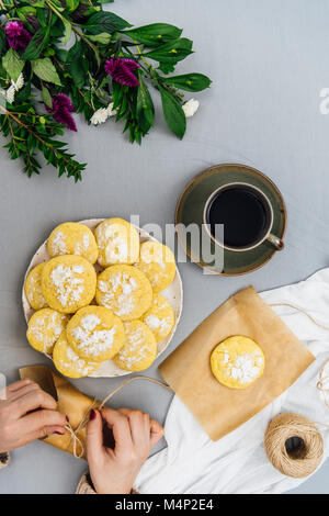Une femme citron cookies et d'enrubannage citron cookies empilés sur une assiette, une tasse de café et de fleurs photographiées en vue de dessus. Banque D'Images