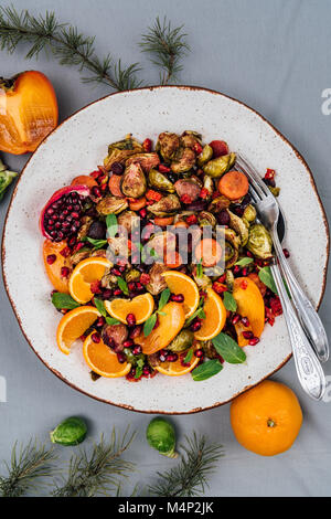 Salade de choux de bruxelles rôtis avec orange, kaki, carotte et grenade arilles servi dans un grand bol à salade photographié en vue de dessus. Deux fourchettes Banque D'Images