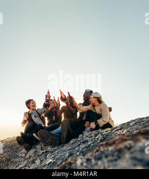 Groupe d'amis sur une montagne à faire la fête avec de la bière. Les jeunes hommes et femmes toasting beers au coucher du soleil. Banque D'Images