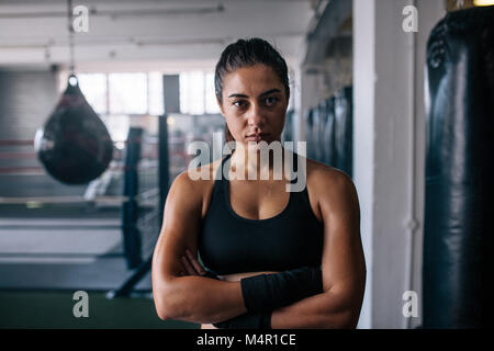 Close up of a female boxer debout à l'intérieur d'un studio de boxe avec ses mains pliées. Femme debout dans un centre d'entraînement de boxe avec sacs de frappe et de bo Banque D'Images