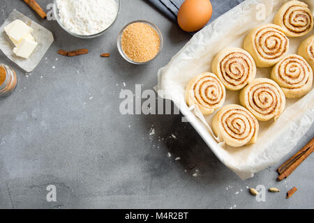 Cannelle ou cinnabon, recette maison pâte crue préparation doux traditionnel dessert brioches avec ingrédients de pâtisserie sur fond noir en gris, cop Banque D'Images