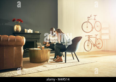 Deux jeunes designers assis dans un bureau moderne et élégante de parler ensemble tout en travaillant avec un ordinateur portable en ligne Banque D'Images