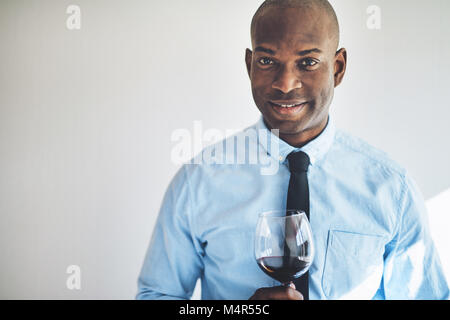 Smiling mature homme africain dans une chemise et cravate de boire un verre de vin rouge Banque D'Images