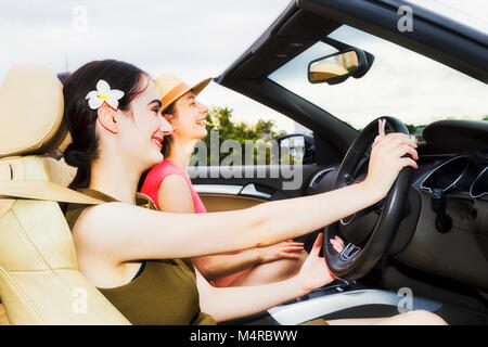 Close-up ouvrir de l'intérieur de luxe moderne roadster sport voiture avec deux jeunes femme jouissant de la liberté et style de vie sous un ciel clair sur une journée ensoleillée d'été Banque D'Images