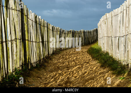 Chemin de sable côtières, barrières en bois foncé dans les deux, et ciel nuageux, en Bretagne, France Banque D'Images