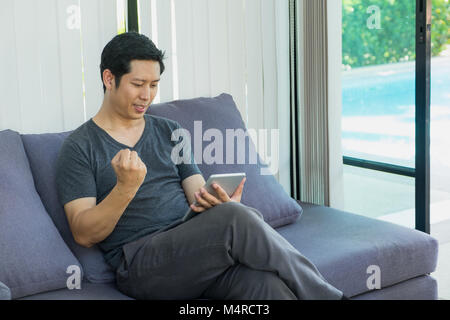 Homme assis sur un canapé et regarder un match de football en direct en streaming sur tablette et jusqu'à bras pour boire de l'équipe.sport digital lifestyle Banque D'Images