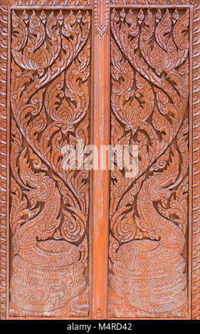 Motif de sculpture avec le dragon symbole dans le style thaï traditionnel sur la porte de bois de l'Eglise thaïlandaise. Banque D'Images