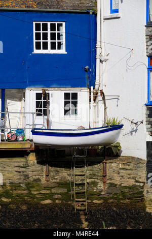 Canot bleu et blanc sur bossoirs contraste avec les murs de maison peint à l'harbourside à Polperro, Cornwall, UK Banque D'Images