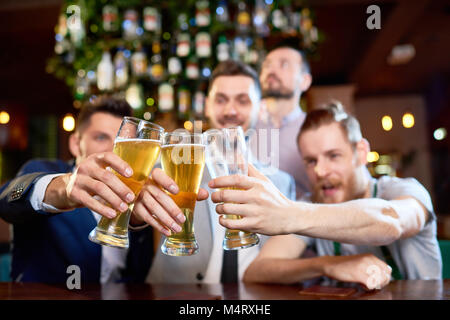 Groupe d'amis joyeux tintement des verres de bière, tandis qu'assis à comptoir bar et la célébration de fin de semaine de travail, l'accent sur le premier plan Banque D'Images