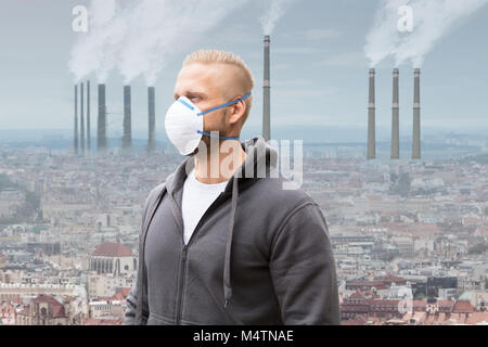 Un homme portant un masque contre la pollution de l'émettant de la fumée des cheminées d'usine Banque D'Images