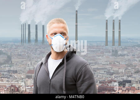 Un homme portant un masque contre la pollution de l'émettant de la fumée des cheminées d'usine Banque D'Images