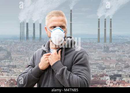 Un homme portant un masque contre la pollution de l'émettant de la fumée des cheminées d'usine Banque D'Images