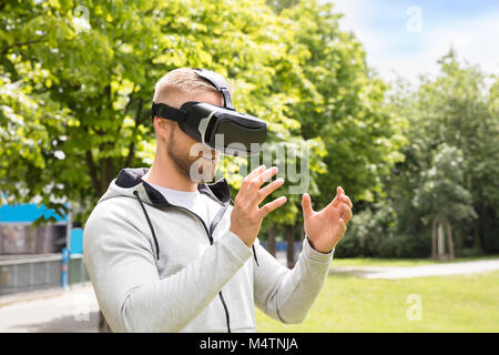 Homme barbu attrayant appréciant la Réalité Virtuelle lunettes dans Park Banque D'Images