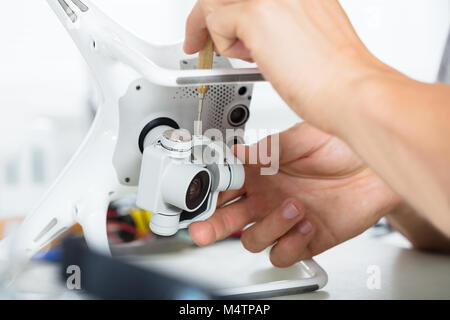 La main du mâle de la réparation de l'appareil photo d'action sur Quadrocopter Drone à table avec l'outil en atelier moderne Banque D'Images