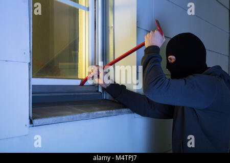 Cambrioleur avec masque noir à l'aide de biche d'entrer par effraction dans une maison la nuit Banque D'Images