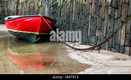 Gros plan d'un petit bateau à ramer rouge enchaîné à marée basse dans le port pittoresque de Portsoy, Aberdeenshire, Écosse, Royaume-Uni, avec des reflets d'eau Banque D'Images