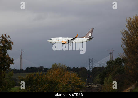 Quelques instants avant l'atterrissage d'un Boeing 737 jt OY-JTT vole au-dessus de la ligne de chemin de fer de Fife Edimbourg avec un train approchant au loin Banque D'Images