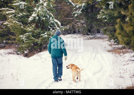 Man with dog walking on snowy forêt de pins en hiver retour à l'appareil photo Banque D'Images